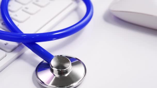 医療コンセプト 白いコンピュータのキーボード上の青い聴診器が付いている医者のオフィスの仕事のテーブル トラック右 クローズアップ マクロショット — ストック動画