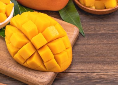 Ahşap kesme tahtası ve rustik ahşap arka plan taze doğranmış mango küpleri. Tropikal yaz meyve konsepti, yakın çekim, makro, kopyalama alanı.