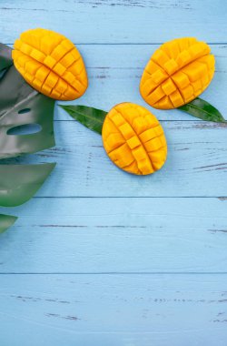 Taze mango - parlak mavi ahşap arka plan üzerinde yeşil yaprakları ile güzel doğranmış meyve. Tropikal meyve tasarım konsepti. Düz yatıyordu. Üst te. Kopyalama alanı