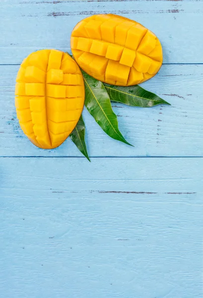 Φρέσκο μάνγκο-όμορφο κομμένο φρούτο με πράσινα φύλλα σε φωτεινό μπλε ξύλινο φόντο. Φιλοσοφία σχεδιασμού τροπικών φρούτων. "Επίπεδη". Κορυφαία προβολή. Αντιγραφή χώρου — Φωτογραφία Αρχείου