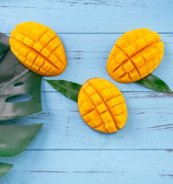 Taze mango - parlak mavi ahşap arka plan üzerinde yeşil yaprakları ile güzel doğranmış meyve. Tropikal meyve tasarım konsepti. Düz yatıyordu. Üst te. Kopyalama alanı