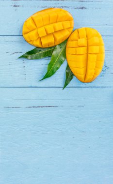 Taze mango - parlak mavi ahşap arka plan üzerinde yeşil yaprakları ile güzel doğranmış meyve. Tropikal meyve tasarım konsepti. Düz yatıyordu. Üst te. Kopyalama alanı