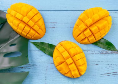 Taze mango - parlak mavi ahşap arka plan üzerinde yeşil yaprakları ile güzel doğranmış meyve. Tropikal meyve tasarım konsepti. Düz yatıyordu. Üst te. Kopyalama alanı