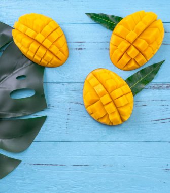 Taze mango - parlak mavi ahşap arka plan üzerinde yeşil yaprakları ile güzel doğranmış meyve. Tropikal meyve tasarım konsepti. Düz yatıyordu. Üst te. Kopyalama alanı