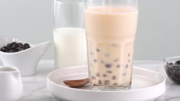 飲みガラスにタピオカパールバブルミルクティーをかき混ぜて 明るい大理石のテーブルの上においしい台湾の人気ドリンク 自家製のコンセプト 4Kショットビデオ — ストック動画