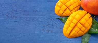 Taze mango-koyu mavi ahşap arka planda yeşil yaprakları ile güzel doğranmış meyve. Tropikal meyve tasarım kavramı. Düz yatıyordu. Üst görünüm. Boşluk Kopyala