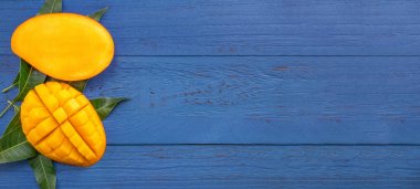 Taze mango-koyu mavi ahşap arka planda yeşil yaprakları ile güzel doğranmış meyve. Tropikal meyve tasarım kavramı. Düz yatıyordu. Üst görünüm. Boşluk Kopyala