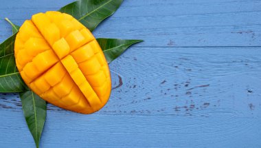 Taze mango-koyu mavi ahşap arka planda yeşil yaprakları ile güzel doğranmış meyve. Tropikal meyve tasarım kavramı. Düz yatıyordu. Üst görünüm. Boşluk Kopyala