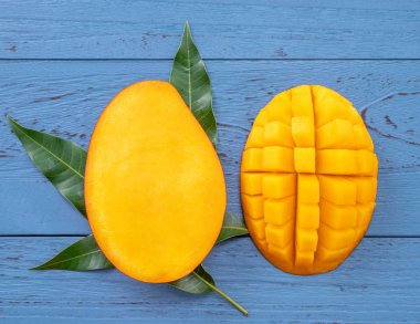 Taze mango-koyu mavi ahşap arka planda yeşil yaprakları ile güzel doğranmış meyve. Tropikal meyve tasarım kavramı. Düz yatıyordu. Üst görünüm. Boşluk Kopyala