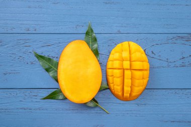 Taze mango-koyu mavi ahşap arka planda yeşil yaprakları ile güzel doğranmış meyve. Tropikal meyve tasarım kavramı. Düz yatıyordu. Üst görünüm. Boşluk Kopyala