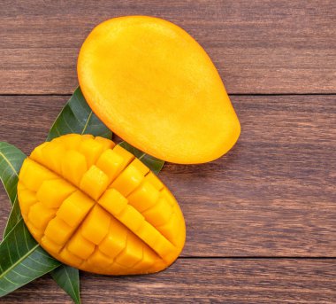 Taze mango-koyu ahşap ahşap arka planda yeşil yaprakları ile güzel doğranmış meyve. Tropikal meyve tasarım kavramı. Düz yatıyordu. Üst görünüm. Boşluk Kopyala