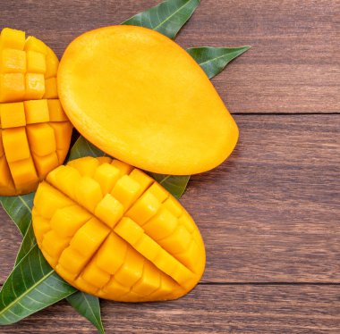 Taze mango-koyu ahşap ahşap arka planda yeşil yaprakları ile güzel doğranmış meyve. Tropikal meyve tasarım kavramı. Düz yatıyordu. Üst görünüm. Boşluk Kopyala