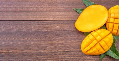 Taze mango-koyu ahşap ahşap arka planda yeşil yaprakları ile güzel doğranmış meyve. Tropikal meyve tasarım kavramı. Düz yatıyordu. Üst görünüm. Boşluk Kopyala