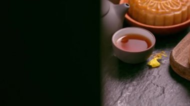 Siyah kayrak arka plan üzerinde çay ve çiçek ile ahşap bir tepsi üzerinde Güzel Moon kek. Çin geleneksel Orta Sonbahar Festivali kavramı. Kamyon sağ.