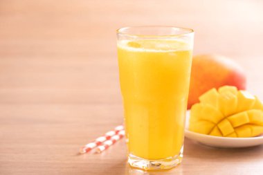 Parlak ahşap masa arka plan üzerinde güzel doğranmış hamuru eti ve saman ile taze mango suyu. Tropikal meyve tasarım konsepti. Kapat, kopyalama alanı.