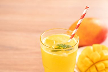 Parlak ahşap masa arka plan üzerinde güzel doğranmış hamuru eti ve saman ile taze mango suyu. Tropikal meyve tasarım konsepti. Kapat, kopyalama alanı.