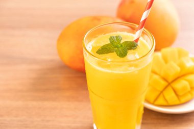 Parlak ahşap masa arka plan üzerinde güzel doğranmış hamuru eti ve saman ile taze mango suyu. Tropikal meyve tasarım konsepti. Kapat, kopyalama alanı.