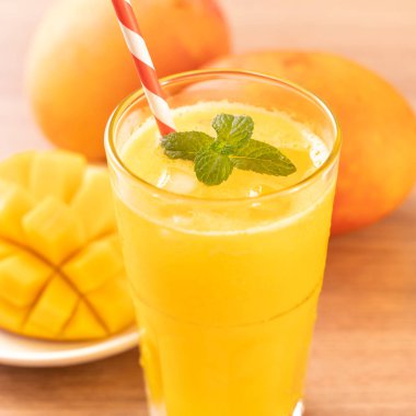 Parlak ahşap masa arka plan üzerinde güzel doğranmış hamuru eti ve saman ile taze mango suyu. Tropikal meyve tasarım konsepti. Kapat, kopyalama alanı.