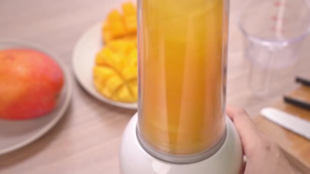 新鲜制作的芒果汁在明亮的木桌背景的夏季厨房 健康女人自制概念 慢动作 — 图库视频影像