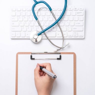 Kadın doktor steteskop, bilgisayar klavyesi ile beyaz çalışma masası üzerinde pano üzerinde tıbbi kayıt durumda yazıyor. Üst görünüm, düz döşeme, kopyalama alanı