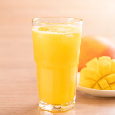Parlak ahşap masa arka plan üzerinde güzel doğranmış hamuru eti ile taze mango suyu. Tropikal meyve içeceği tasarım konsepti. Kapat, kopyalama alanı.