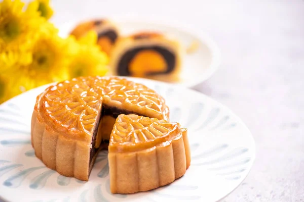 Mid-Autumn Festival traditional food concept - Beautiful cut moon cake on blue pattern plate on white background with flower, close up, copy space — Stock Photo, Image