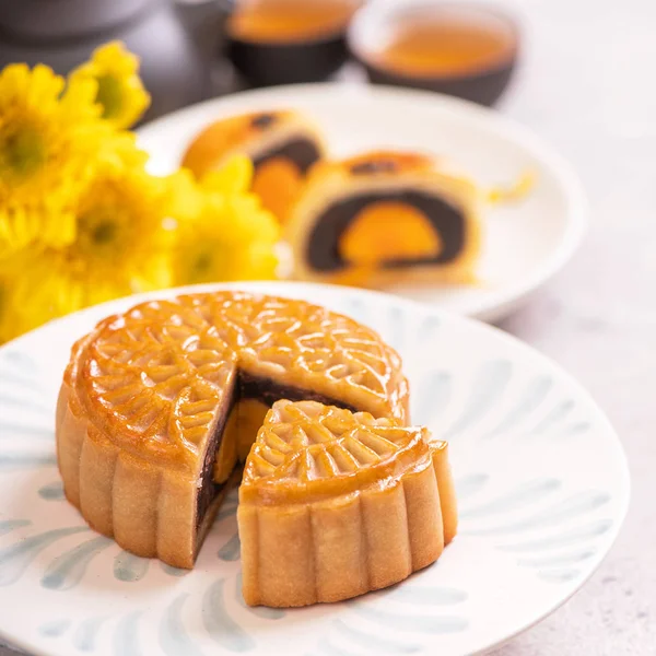 Mid-Autumn Festival traditional food concept - Beautiful cut moon cake on blue pattern plate on white background with flower, close up, copy space — Stock Photo, Image