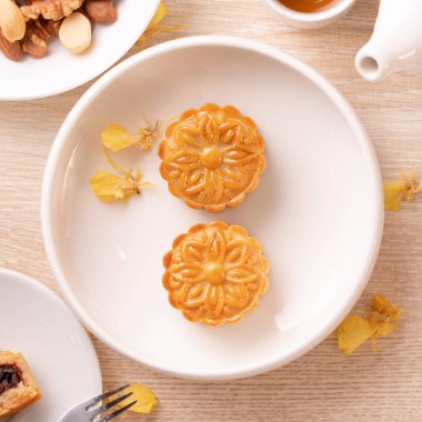 Parlak ahşap masa üzerinde Sonbahar ortası festivali için lezzetli ay pastası, sarı çiçeklerle süslenmiş şenlikli ikindi çayı kavramı, üst görünüm, düz yatıyordu.