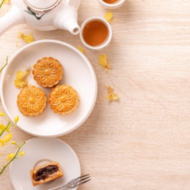 Parlak ahşap masa üzerinde Sonbahar ortası festivali için lezzetli ay pastası, sarı çiçeklerle süslenmiş şenlikli ikindi çayı kavramı, üst görünüm, düz yatıyordu.