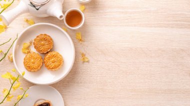 Tasty moon cake for Mid-Autumn festival on bright wooden table, concept of festive afternoon tea decorated with yellow flowers, top view, flat lay. clipart