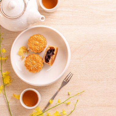 Parlak ahşap masa üzerinde Sonbahar ortası festivali için lezzetli ay pastası, sarı çiçeklerle süslenmiş şenlikli ikindi çayı kavramı, üst görünüm, düz yatıyordu.