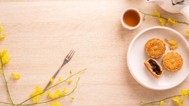 Parlak ahşap masa üzerinde Sonbahar ortası festivali için lezzetli ay pastası, sarı çiçeklerle süslenmiş şenlikli ikindi çayı kavramı, üst görünüm, düz yatıyordu.