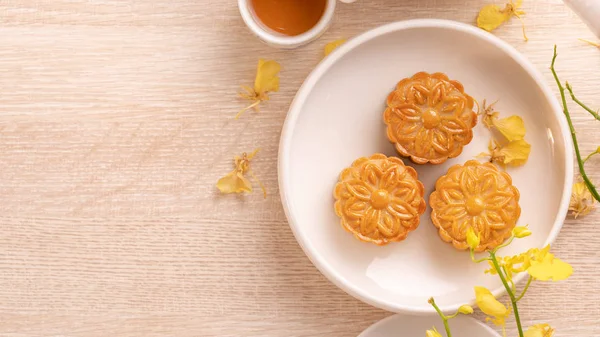 Tasty moon cake for Mid-Autumn festival on bright wooden table, concept of festive afternoon tea decorated with yellow flowers, top view, flat lay. — Stock Photo, Image