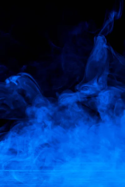Konceptuell bild av blå rök isolerad på mörk svart bakgrund och träbord. — Stockfoto