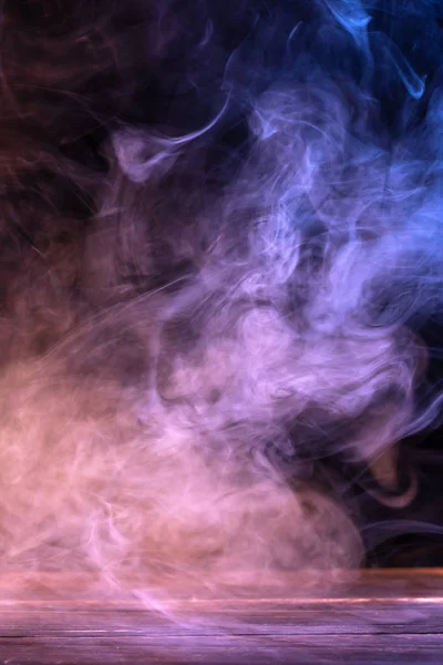 Immagine concettuale di fumo multicolore isolato su sfondo nero scuro e tavolo in legno. — Foto Stock