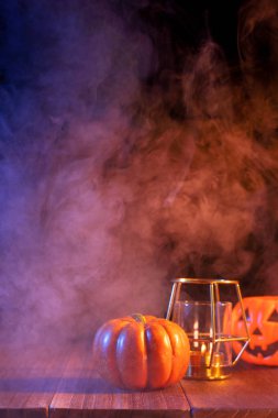 Cadılar Bayramı konsepti, turuncu kabak fener ve arka plan etrafında yeşil-turuncu duman ile koyu ahşap bir masa üzerinde mumlar, hile veya tedavi, yakın