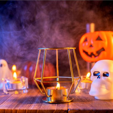 Cadılar Bayramı konsepti, turuncu kabak fener ve arka plan etrafında yeşil-turuncu duman ile koyu ahşap bir masa üzerinde mumlar, hile veya tedavi, yakın