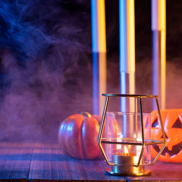 Cadılar Bayramı konsepti, turuncu kabak fener ve arka plan etrafında yeşil-turuncu duman ile koyu ahşap bir masa üzerinde mumlar, hile veya tedavi, yakın