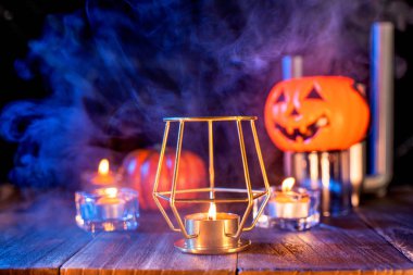 Cadılar Bayramı konsepti, turuncu kabak fener ve arka plan etrafında yeşil-turuncu duman ile koyu ahşap bir masa üzerinde mumlar, hile veya tedavi, yakın