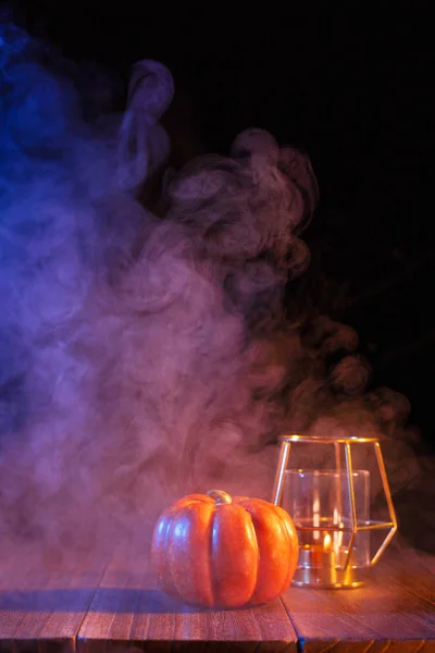 Απόκριες ιδέα, πορτοκαλί φανάρι κολοκύθα και κεριά σε ένα σκούρο ξύλινο τραπέζι με μπλε-πορτοκαλί καπνό γύρω από το φόντο, τέχνασμα ή κέρασμα, κοντινό — Φωτογραφία Αρχείου