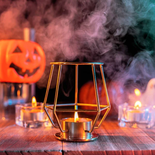 Cadılar Bayramı konsepti, turuncu kabak fener ve arka plan etrafında yeşil-turuncu duman ile koyu ahşap bir masa üzerinde mumlar, hile veya tedavi, yakın