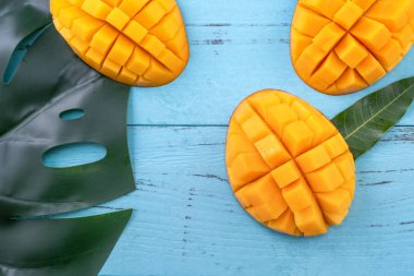 Taze mango - parlak mavi ahşap arka plan üzerinde yeşil yaprakları ile güzel doğranmış meyve. Tropikal meyve tasarım konsepti. Düz yatıyordu. Üst te. Kopyalama alanı
