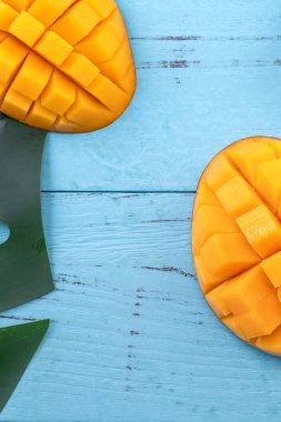Taze mango - parlak mavi ahşap arka plan üzerinde yeşil yaprakları ile güzel doğranmış meyve. Tropikal meyve tasarım konsepti. Düz yatıyordu. Üst te. Kopyalama alanı