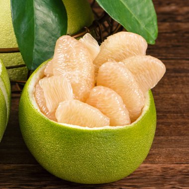 Taze soyulmuş pomelo, greyfurt, koyu ahşap tahta masada yeşil yaprakları ile gölgeli. Sonbahar ortası festivaline yakın mevsim meyveleri, yakın çekim, kopyalama alanı