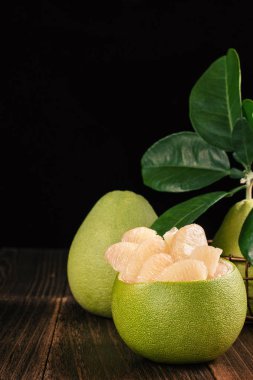 Fresh peeled pomelo, grapefruit, shaddock with green leaves on dark wooden plank table. Seasonal fruit near mid-autumn festival, close up, copy space clipart