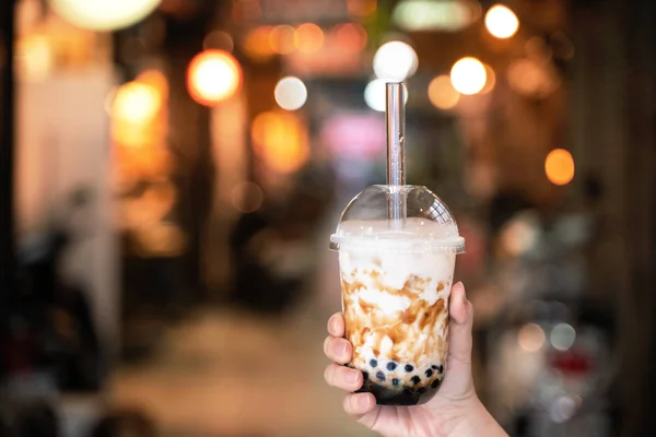 Chica joven en chaqueta de mezclilla está bebiendo azúcar morena con sabor a tapioca perla té de leche de burbuja con paja de vidrio en el mercado nocturno de Taiwán, de cerca, bokeh — Foto de Stock