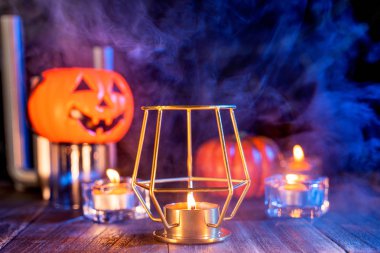 Cadılar Bayramı konsepti, turuncu kabak fener ve arka plan etrafında mavi-turuncu duman ile koyu ahşap bir masa üzerinde mumlar, hile veya tedavi, yakın