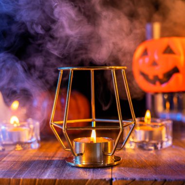 Cadılar Bayramı konsepti, turuncu kabak fener ve arka plan etrafında mavi-turuncu duman ile koyu ahşap bir masa üzerinde mumlar, hile veya tedavi, yakın