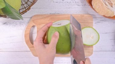 Genç asyalı kadın parlak beyaz ahşap masa ve doğrama tahtası üzerinde ev mutfağında yemek için taze pomelo kesiyor, üst görünümü, havai görünüm, yaşam tarzı.
