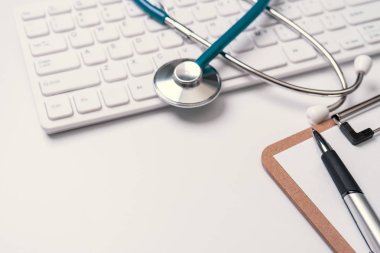 Doktor kavramı teşhis - tıbbi kayıt durumda bilgisayar klavyesi üzerinde stetoskop ve beyaz çalışma masasında kalem. Üst görünüm, düz döşeme, kopyalama alanı
